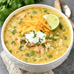 Easy green chile chicken enchilada soup is shown in a bowl, garnished with cilantro and a dollop of sour cream, making it a comforting and flavorful meal.